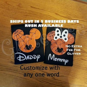 May include: Two black t-shirts with a spiderweb design and the words "Daddy" and "Mommy" printed on them. The shirts are decorated with orange and black glitter.