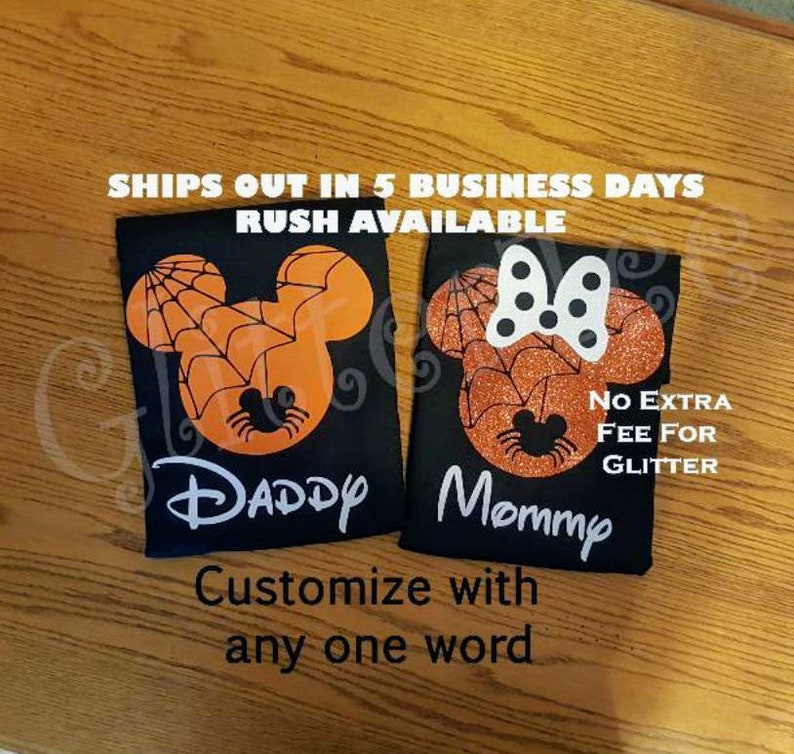 May include: Two black t-shirts with a spiderweb design and the words "Daddy" and "Mommy" printed on them. The shirts are decorated with orange and black glitter.