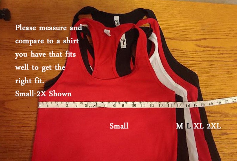 May include: Four tank tops in different sizes, laid out on a wooden surface. The tank tops are red, white, black, and black. A measuring tape is placed across the bottom of the tank tops, with the numbers 2 through 22 visible. The text "Small-2X Shown" is written above the measuring tape. The text "Small" is written below the red tank top. The text "M L XL 2XL" is written below the measuring tape.
