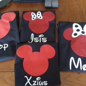May include: Four black t-shirts with red Mickey Mouse head designs. One shirt has "Pop" in white, another has "Isis", a third has "Xzius", and the last has "Mom". The Minnie Mouse heads have white bows and glitter.