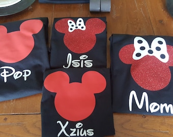 May include: Four black t-shirts with red Mickey Mouse head designs. One shirt has "Pop" in white, another has "Isis", a third has "Xzius", and the last has "Mom". The Minnie Mouse heads have white bows and glitter.