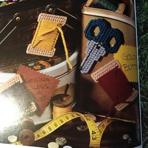 Peut inclure: Gros plan sur une collection de fournitures artisanales, comprenant une bobine de fil jaune, une paire de ciseaux bleus, une bobine de fil rouge, une pancarte de cours de couture et un mètre ruban jaune. Les articles sont disposés sur une surface brune avec un fond vert.