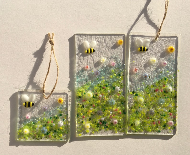May include: Three glass panels featuring a floral design and a bee. The panels are of varying sizes and are hung with twine.