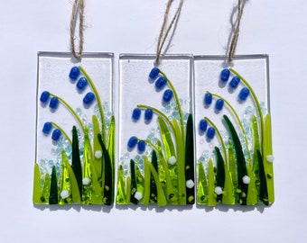 May include: Three glass ornaments featuring blue and green glass flowers on a white background. Each ornament has a string for hanging.