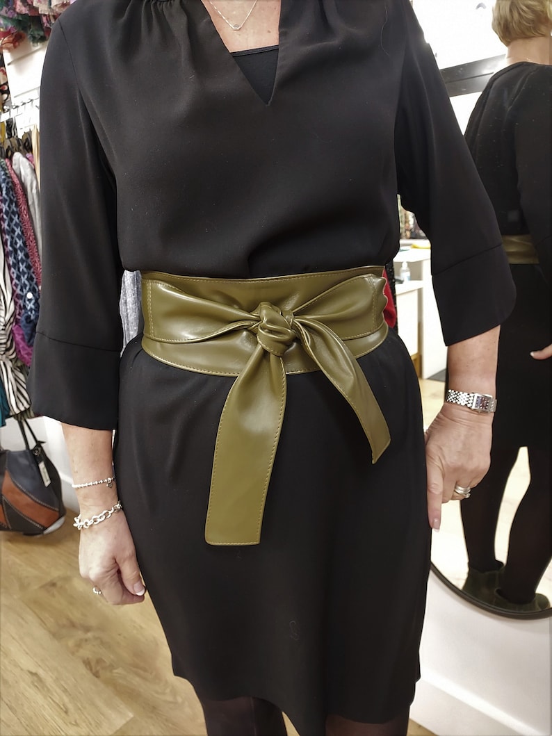 an olive green leather obi belt tied around the waist of a lady wearing a black dress.