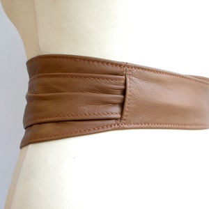 May include: A brown leather belt with a wide, folded design. The belt is stitched with a light brown thread.