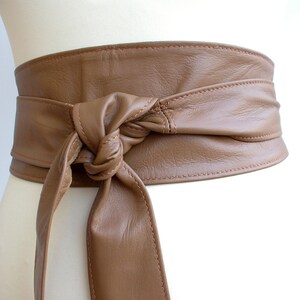 May include: A brown leather belt with a knotted tie. The belt is wide and has a stitched edge.