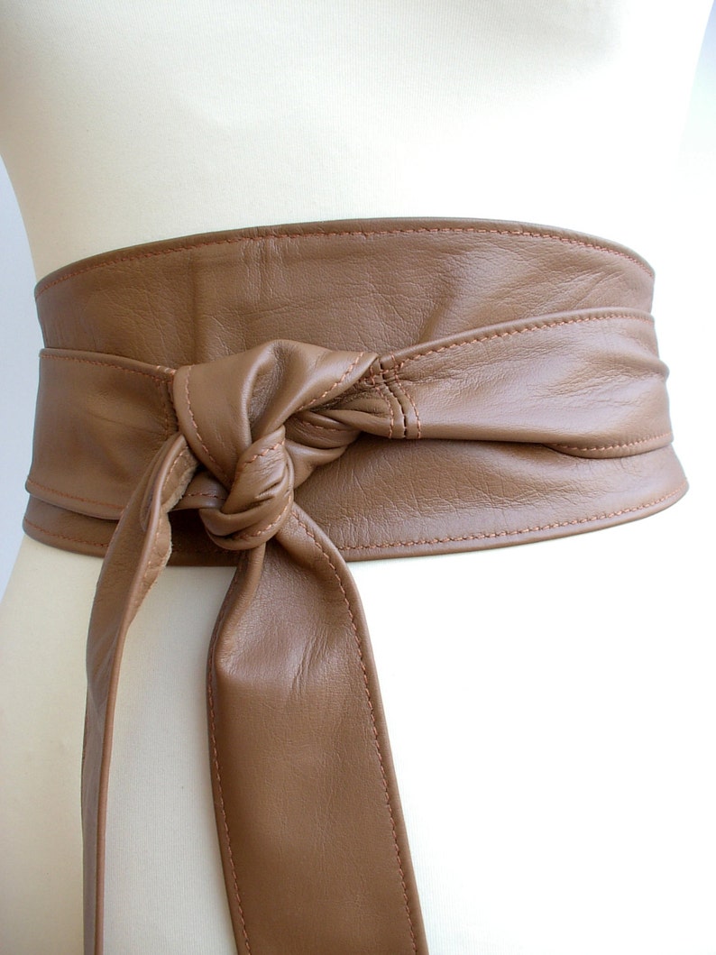 May include: A brown leather belt with a knotted tie. The belt is wide and has a stitched edge.