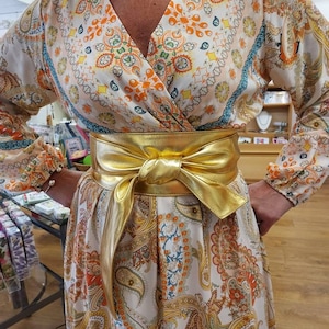 a gold leather obi belt tied around the waist of a lady wearing a patterned dress.