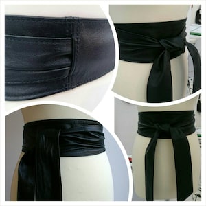 May include: A black leather obi belt with a wide, gathered design. The belt is shown tied in multiple ways, with long, flowing ties. The leather appears smooth and has a slight sheen, suggesting a high-quality material.