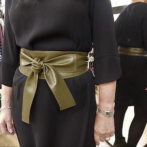 May include: A black dress with a wide, olive green faux leather belt tied in a bow at the front.