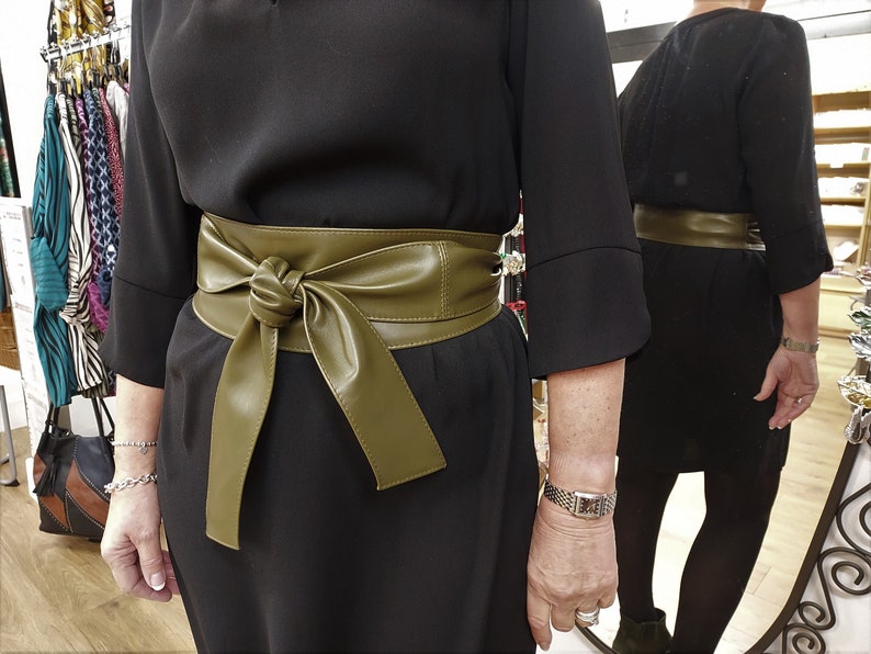 May include: A black dress with a wide, olive green faux leather belt tied in a bow at the front.