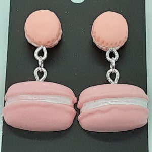 May include: A pair of pink macaron dangle earrings with silver chains. The macarons have a white filling.