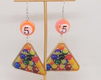 May include: A pair of dangle earrings featuring a pink and orange ball with the number "5" on it and a clear triangle-shaped charm with a printed image of a pool ball rack.