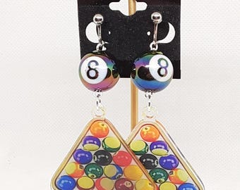 May include: A pair of iridescent black and white 8-ball earrings with a clear triangle charm featuring a pool ball rack.