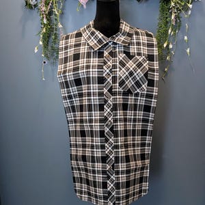 May include: A sleeveless button-up shirt with a black and white plaid pattern. The shirt has a single chest pocket and a collared neckline.