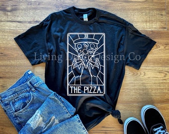 May include: Black t-shirt with a white graphic of a pizza slice held by hands, framed within a rectangle. The text "THE PIZZA" is below the graphic. Blue jeans and black and white sneakers are also in the image.