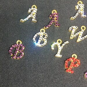 Può includere: Ciondoli con alfabeto in metallo dorato incastonati con strass. Le lettere includono A, B, Y, P e Z, in vari colori come trasparente, viola e rosso. Ogni ciondolo ha un piccolo anello per il fissaggio a gioielli o artigianato.