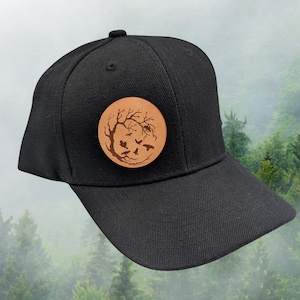 May include: Black baseball cap with a brown leather patch featuring a tree with birds flying around it.