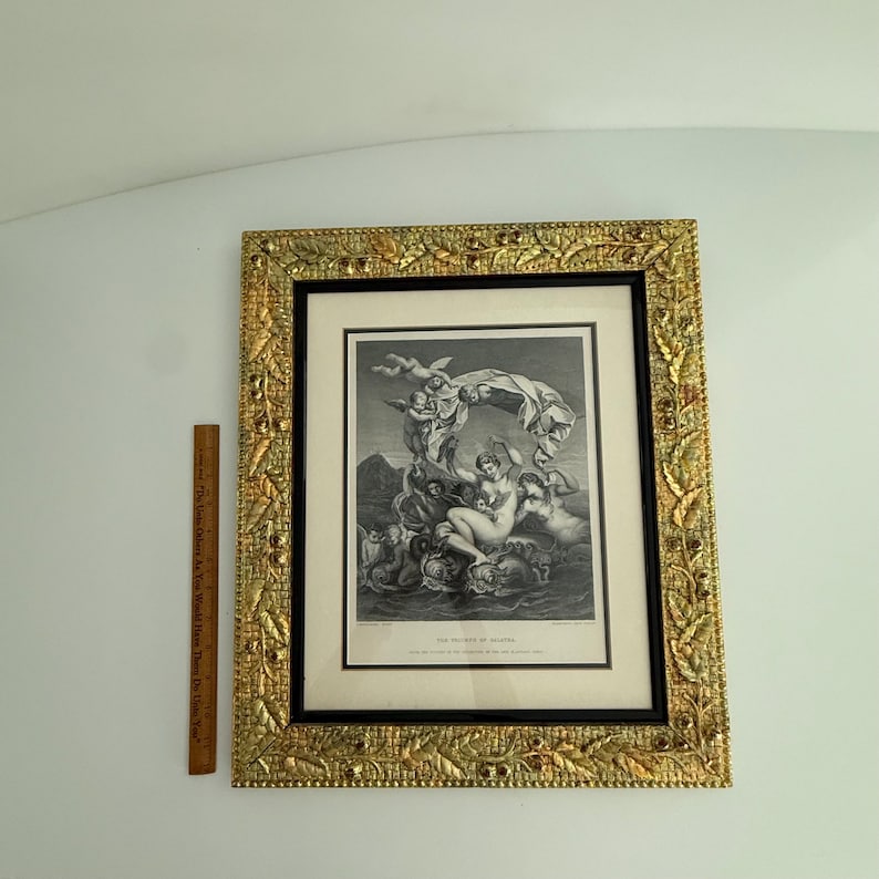 Puede incluir: Impresi&oacute;n en blanco y negro enmarcada de una escena cl&aacute;sica, con figuras y querubines. La impresi&oacute;n est&aacute; enmarcada en un passe-partout negro y un marco dorado ornamentado. Una regla de madera est&aacute; colocada junto al marco.
