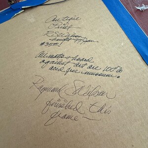 Puede incluir: Tablero de respaldo envejecido, de color canela, con texto manuscrito en tinta negra. El texto incluye las palabras "Coutique Frisch", "RSWilson" y "Raymond S Wilson". Cinta adhesiva azul visible en los bordes.