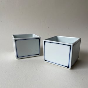 Puede incluir: Dos cuencos cuadrados de cerámica blanca con un borde azul y negro alrededor del borde.