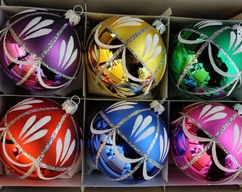 May include: Six colorful Christmas ornaments in a box. Each glass ball is a different color: purple, yellow, green, red, blue, and pink. The ornaments have a white and silver design.