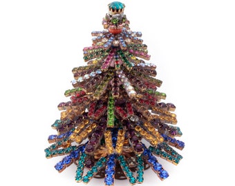 May include: A colorful jeweled Christmas tree ornament with a star on top. The tree is made of metal and is covered in rhinestones of various colors, including red, green, blue, purple, and gold.