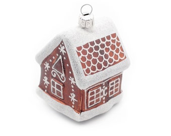 May include: A brown and white gingerbread house Christmas ornament with a snowy roof and a silver hanger.