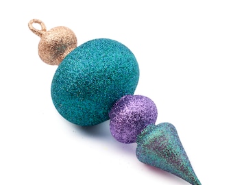 Puede incluir: Un adorno para la cima del árbol de Navidad de color turquesa, morado y dorado con purpurina y punta puntiaguda.