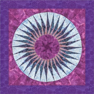 Op de afbeelding: Een paarse en blauwe quilt met een groot, cirkelvormig ontwerp in het midden. Het ontwerp heeft een zonnestralenpatroon met een kleinere cirkel in het midden.