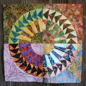 May include: A quilt made of colorful fabric squares with a spiral pattern in the center. The quilt is made of various shades of green, blue, purple, orange, and brown.