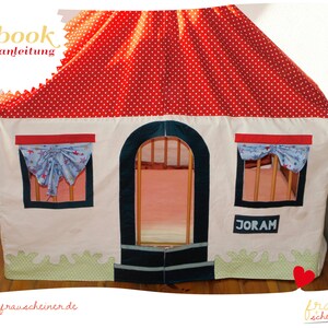May include: A white playhouse with a red polka-dot roof and blue star-patterned curtains. The house has a green grass-like trim and the name "JORAM" is displayed on the side. The text "Ebook" and "Nahanleitung" are visible on the top left.