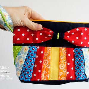 May include: A colorful patchwork clutch with a red polka dot bow and a wrist strap. The clutch features a variety of patterned fabrics in red, blue, green, and yellow. The zipper is yellow.