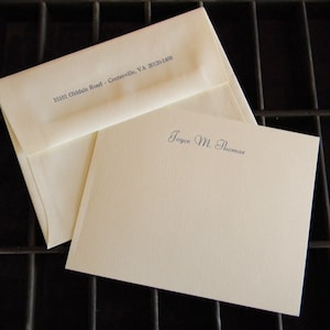 May include: A white envelope with the address "15101 Olddale Road - Centreville, VA 20120-1408" printed on the front. A white card with the name "Joyce M. Thomas" printed in blue ink.