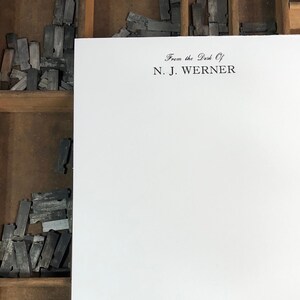 May include: A white sheet of paper with the text "From the Desk of N.J. Werner" printed at the top. The paper is sitting in a wooden drawer filled with metal letterpress type.
