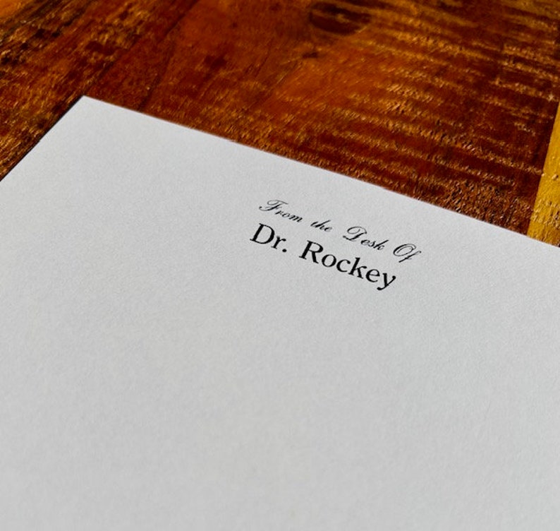 May include: A white piece of paper with the text "From the Desk Of Dr. Rockey" printed in black ink.