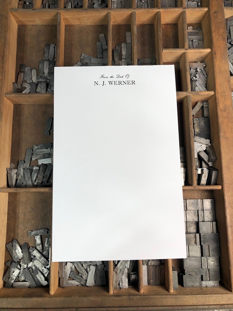 May include: A white sheet of paper with the text "From the Desk of N.J. Werner" printed at the top. The paper is sitting in a wooden drawer filled with metal letterpress type.