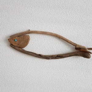 Pode incluir: Uma escultura de peixe de madeira feita de madeira flutuante com um olho de pedra turquesa.