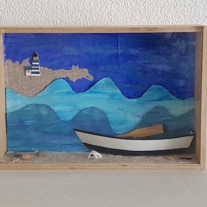 Może przedstawiać: Drewniana skrzynka cieni z niebiesko-białą sceną morskiego krajobrazu. Scena zawiera mały biały statek z brązowym wiosłem, latarnię morską i niebieskie fale.