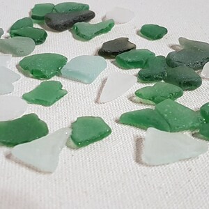 May include: A collection of sea glass in various shades of green and white. The sea glass is smooth and polished, with a variety of shapes and sizes.
