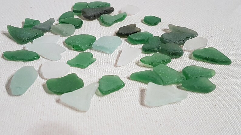 May include: A collection of sea glass in various shades of green and white. The sea glass is smooth and polished, with a variety of shapes and sizes.