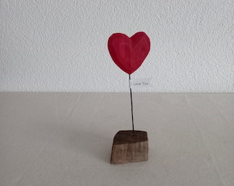 Escultura de madera flotante con corazón rojo.