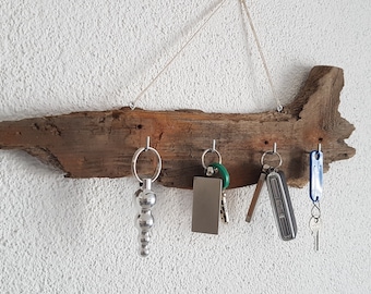 Può includere: Un portachiavi in legno rustico con cinque ganci, appeso a un muro bianco. Il portachiavi è realizzato con un pezzo di legno di deriva e ha una finitura naturale e invecchiata. Ci sono chiavi e portachiavi appesi ai ganci.
