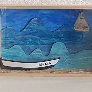 Może przedstawiać: Drewniana ramka z cieniowaniem przedstawiająca morski krajobraz w kolorze niebieskim i zielonym. Na pierwszym planie znajduje się biała łódź z napisem "IRELLA" na boku. Na drugim planie widoczny jest mniejszy żaglowiec.