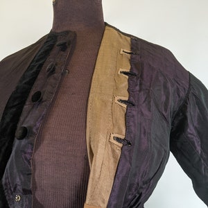 May include: A vintage jacket displayed on a mannequin. The jacket features a dark purple iridescent fabric with black velvet accents and large black buttons. The interior lining is a tan color, and the jacket has a fitted waist.