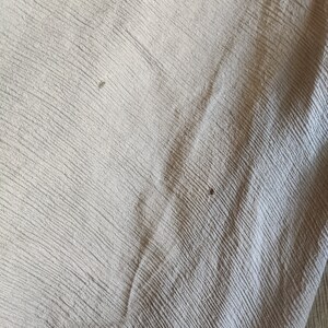 May include: Close-up of a light gray fabric with a subtle textured pattern. The fabric has a slight sheen and appears to be soft and smooth.