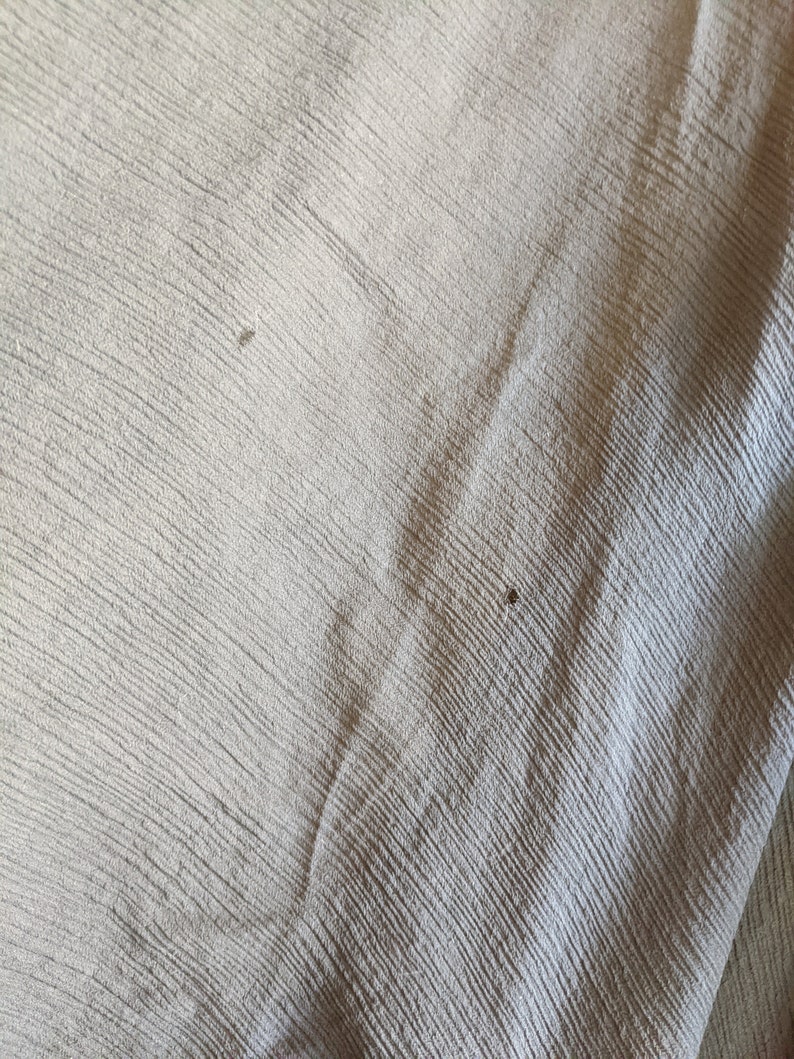 May include: Close-up of a light gray fabric with a subtle textured pattern. The fabric has a slight sheen and appears to be soft and smooth.