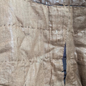 May include: Close-up of a section of brown fabric with visible stitching. The fabric appears to be textured and has a slightly metallic sheen. The stitching is in a darker brown thread, creating a grid-like pattern.