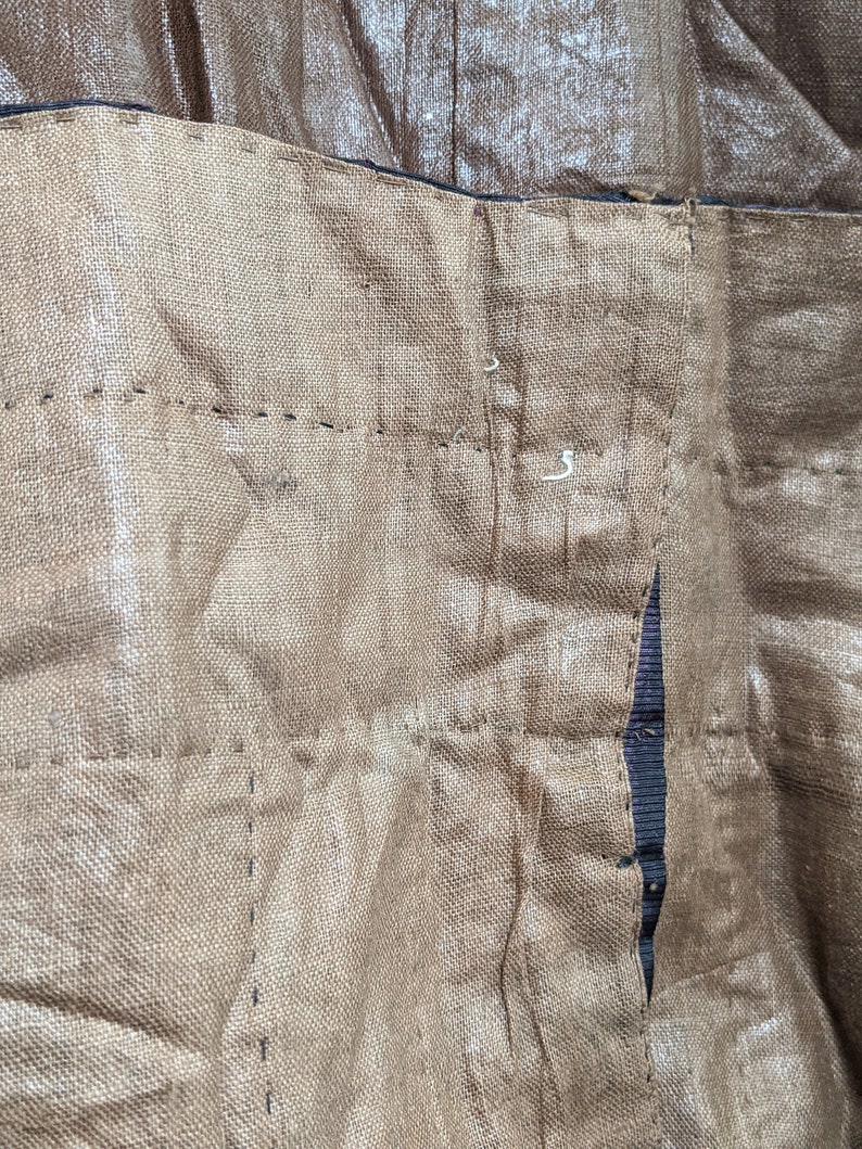 May include: Close-up of a section of brown fabric with visible stitching. The fabric appears to be textured and has a slightly metallic sheen. The stitching is in a darker brown thread, creating a grid-like pattern.